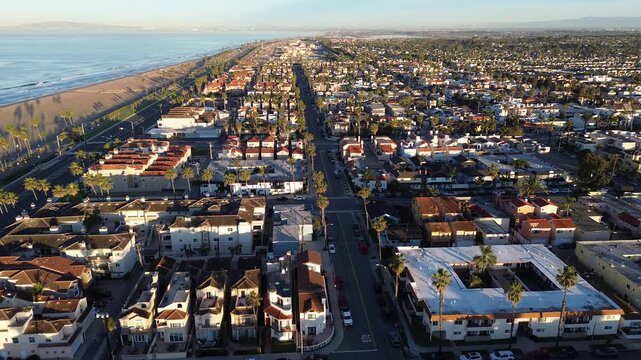 Panoramic landscape shows luxury coastal real estate layouts in Huntington Beach, California. Morning light illuminates premier beachside roads by high-end residential blocks red clay roof tiles