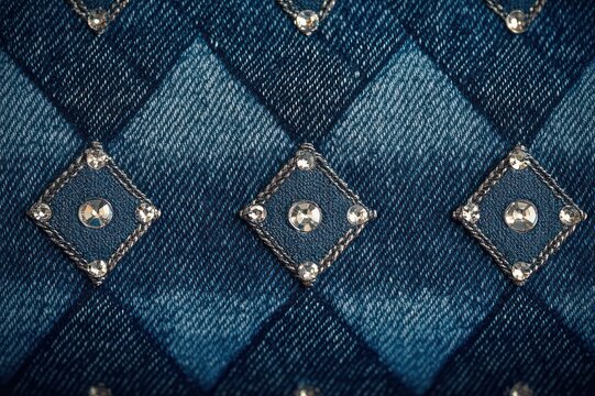 close-up of quilted denim diamond pattern with sewn rhinestone studs, alternating indigo tones and sparkling embellished texture conveying playful glamour