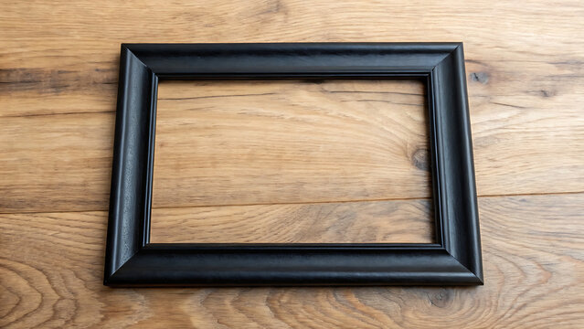 Empty black picture frame on wooden surface. Minimalist blank photo frame for wall decor and custom artwork display.