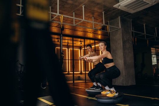 Women doing squats on bosu balls in gym