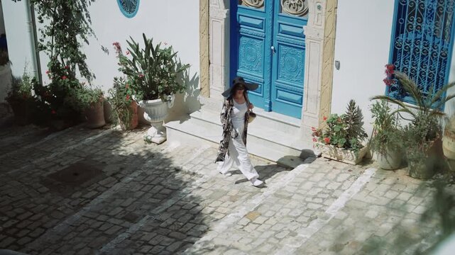 Woman in Hat Walks Down Cobblestone Street in Sidi Bou Said, Tunisia