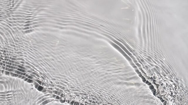 Multiple waves of water cross each other and reflections sunlight in slow motion. Shadow effect. Ripples spontaneously on white background. Beauty shot for skin care cosmetics advertisement. 4k