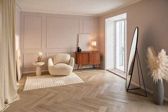 A modern minimalist living room features a cozy boucle armchair, wooden sideboard, floor mirror, and soft neutral decor. Warm natural light fills the elegant interior, creating a calm home.
