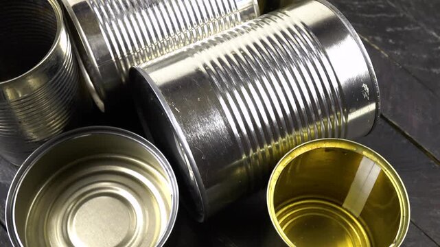 Different empty steel cans for storage of food are on a black wooden board, top view