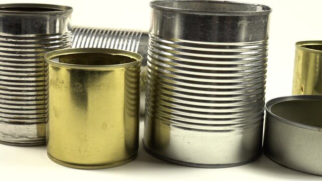Different empty steel cans for storage of food are on a white table, side view