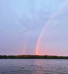 Obraz premium Double rainbow over calm lake after rain with forest on the horizon