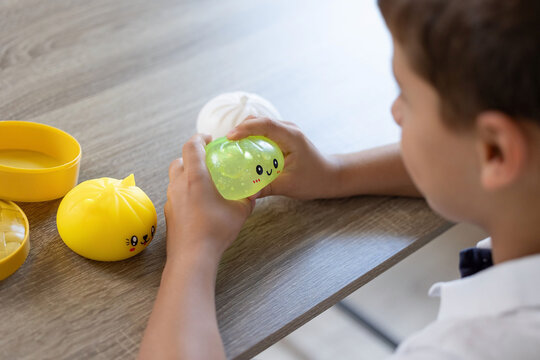 Close view of child hands squeezing translucent green squishy toy while yellow toy parts rest on wood grain table, soft daylight, playful indoor scene, sensory activity, bright colors and relaxed mood