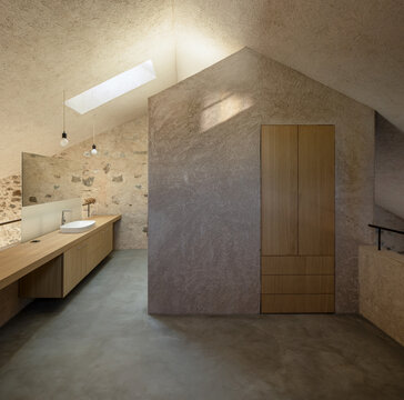 The interior of a bedroom with a bedside table and a washbasin inside it, and a wall behind which the bathroom is located.