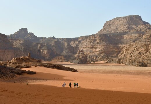 Adventurers walking through the ochre-colored sand of the Sahara Desert in Tassili n'Ajjer Park, Algeria