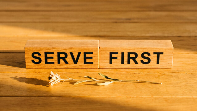 Wooden blocks spelling Serve First on warm wooden plank surface wide, servant leadership concept, service oriented business philosophy