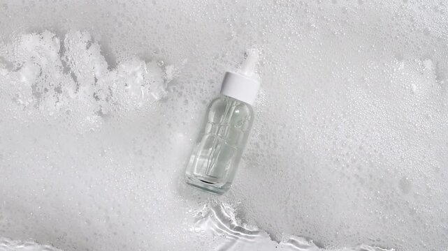 Bottle with a pipette for collagen serum, oil, toner on water texture background surface with bubbles of white soapy foam. Medical skin care. Packaging for design, advertising of a cosmetic product.4k