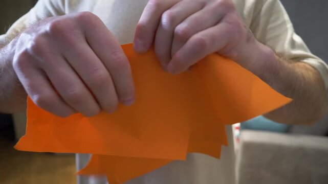A man's hands are tearing a sheet of orange cardboard. Tearing an A4 sheet of paper.