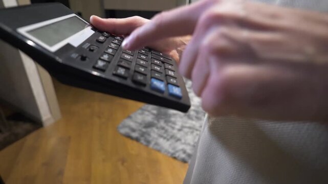 A close-up of a man's hands calculating on an electronic calculator, pressing the buttons with a finger. Calculating a household financial report
