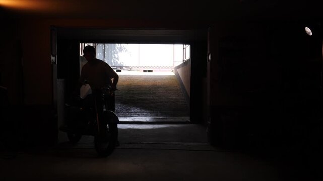 Man pushing a classic 1970s motorcycle into bright light, creating a strong silhouette effect and capturing a moment of transition and journey
