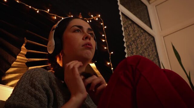 Low angle view of a young Caucasian woman wearing headphones, listening to music and staring blankly into the distance while repeatedly touching her braided hair. Anxiety, neurotic behavior