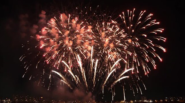 Red and white fireworks burst over city skyline at night