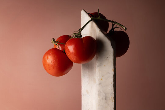 Grappolo di pomodori rossi su elemento in marmo bianco e fondo rosato, natura morta minimalista con spazio per il testo