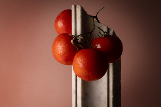 Grappolo di pomodori rossi su elemento in marmo bianco e fondo rosato, natura morta minimalista con spazio per il testo