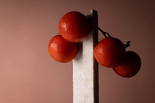 Grappolo di pomodori rossi su elemento in marmo bianco e fondo rosato, natura morta minimalista con spazio per il testo