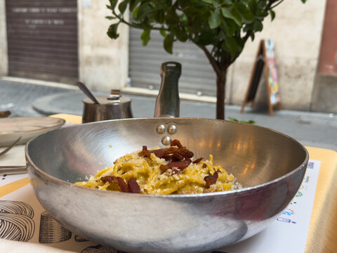 Authentic Italian pasta carbonara with crispy guanciale served in a traditional metal pan on an outdoor restaurant table in Rome, Italy.