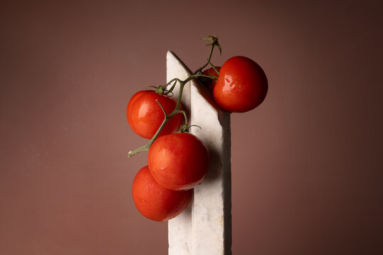Grappolo di pomodori rossi su elemento in marmo bianco e fondo rosato, natura morta minimalista con spazio per il testo
