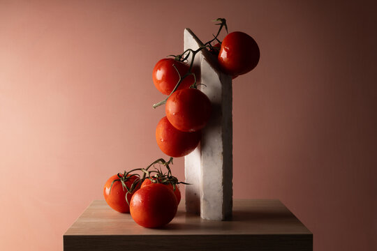 Grappolo di pomodori rossi su elemento in marmo bianco e fondo rosato, natura morta minimalista con spazio per il testo