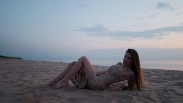 Young woman reclining on sandy beach at dusk beneath soft pastel sky and calm horizon