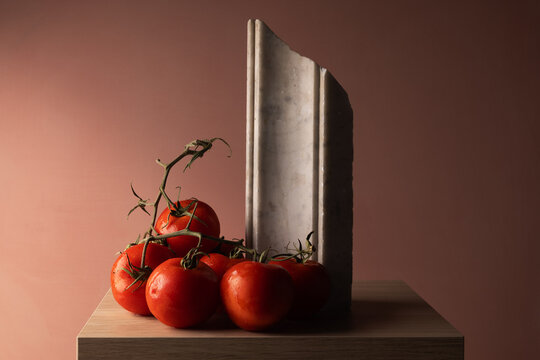 Grappolo di pomodori rossi su elemento in marmo bianco e fondo rosato, natura morta minimalista con spazio per il testo