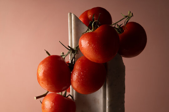 Grappolo di pomodori rossi su elemento in marmo bianco e fondo rosato, natura morta minimalista con spazio per il testo