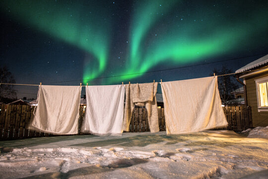 Laundry Drying on a Line Beneath Green Aurora in Snowy Yard