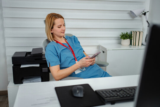 Nurse wearing scrubs sitting at desk checking smartphone