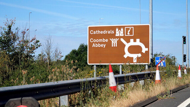 Brown tourist road sign, roundabout direction sign pointing to Cathedrals and Coombe Abbey on UK highway with traffic cones