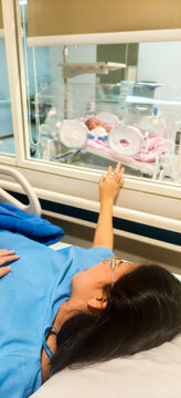 Mother Lying in Hospital Bed Reaching Out Toward Newborn Baby in Incubator