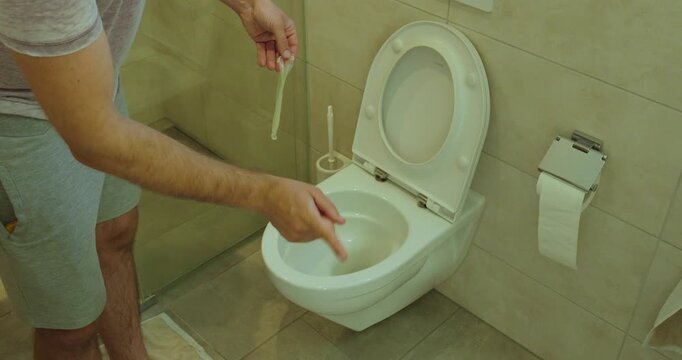 Person holding a used condom near a toilet, showing proper disposal awareness and preventing bathroom plumbing problems.