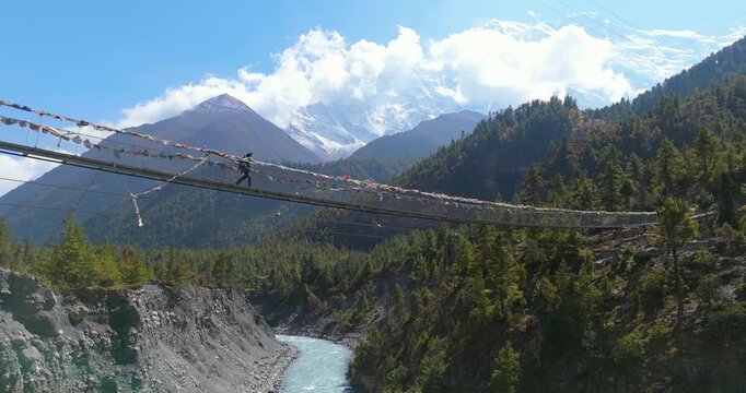 Annapurna circuit, Manang, Nepal, Drone shot, of a male trekker across a suspension bridge, the snow-capped Annapurna II, turquoise river winds through a steep-sided canyon
