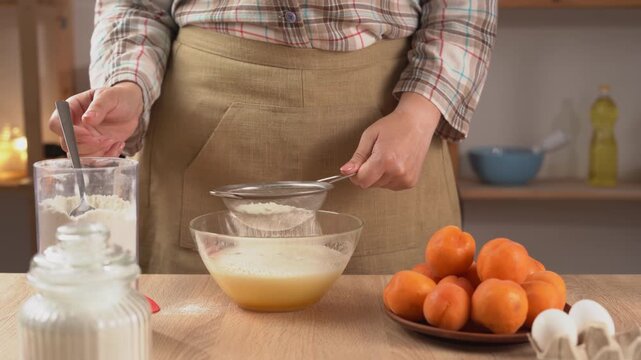 Pastry chef woman sieves flour into egg batter in a glass bowl while preparing dough for homemade baking.