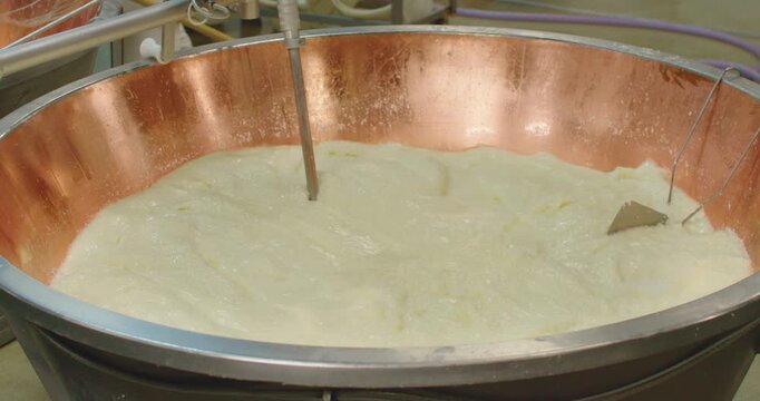 Slow Motion Of Professional dairy mixer processing fresh milk inside a large copper vat in a cheese factory. Industrial Mixer Processing Fresh Milk in Copper Cheese Vat