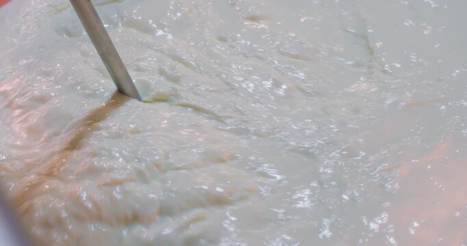 Slow Motion Of Mechanical stirring rod mixing fresh cheese curd in a traditional copper vat during dairy production. Cheese Curd Stirred inside Large Copper Dairy Vat.