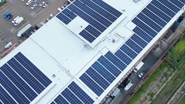 Rows of blue photovoltaic panels blanket a large retail building roof while delivery trucks move along the service bay below.