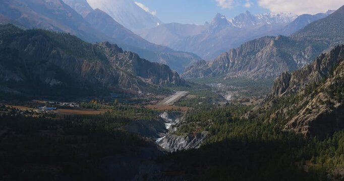 Annapurna Circuit, Humde, Manang Nepal, drone aerial shot overlooking the mountain airport runway situated in a deep pine forest valley alongside the Marsyangdi River bed.