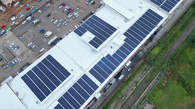 Large solar panel arrays cover the roof of a shopping mall beside parking and rail lines in Orange Farm, South Africa.