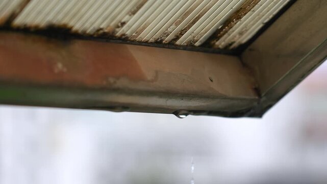 Close-up of water drops falling slowly from the edge of the eaves after the rain
