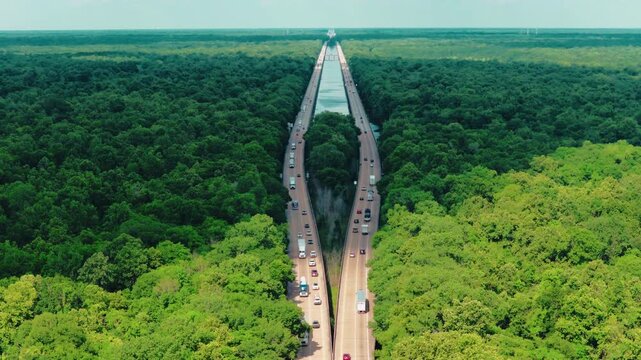 Aerial over the Atchafalaya Basin, the largest river swamp in America, as twin interstate spans thread through miles of unbroken Louisiana wetland forest toward the horizon. I-10