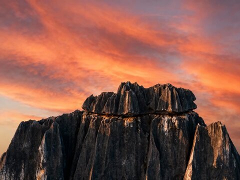 A dramatic rock formation silhouetted against a fiery orange and red sunset sky