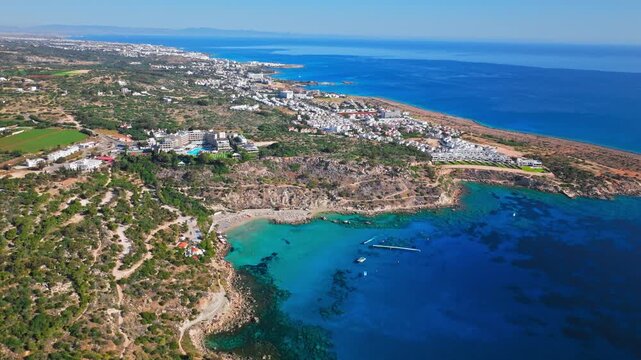 Drone view of Konnos Bay, Cyprus. Clear blue water, rocky coastline and green hills form a peaceful coastal nature scene.