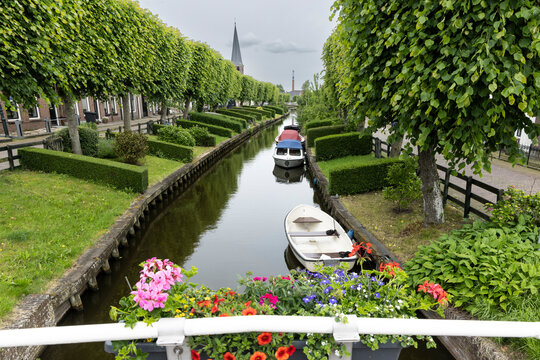Canal with boats and flower boxes in IJlst, Friesland, Netherlands lined by trees and trimmed hedges