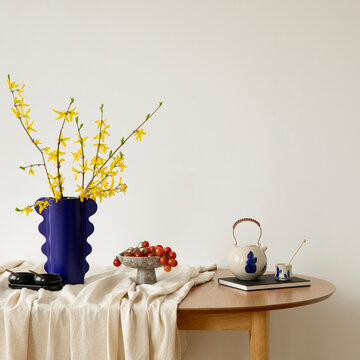 Minimalist dining area with wooden table, linen cloth and bold blue vase of yellow flowers. Bright and elegant modern composition.
