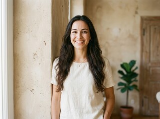 Fototapeta premium Happy young woman with long brown hair smiling while standing in a bright modern home interior with a green wall and plant