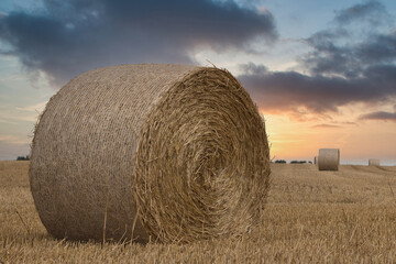 Dramatic sunset sky with dark clouds over a large round straw bale in a harvested wheat field, cinematic rural landscape © vafn
