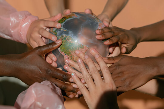 Diverse hands holding a small earth globe against a warm backdrop, representing global unity and multicultural collaboration for environmental care